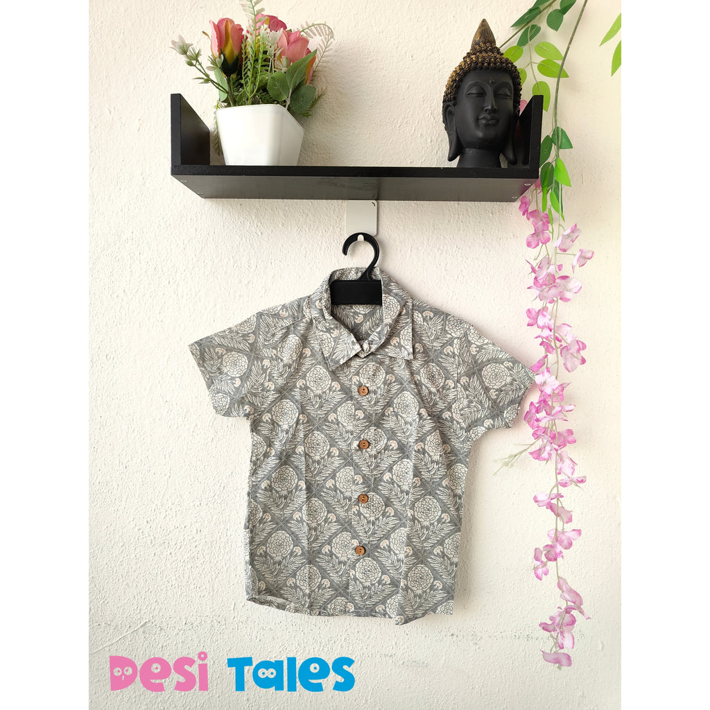 Short-sleeve shirt with floral pattern hanging on a hook against a white wall with decorative elements.